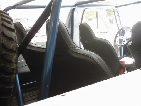 1978 Ford Bronco - The interior of a vehicle shows black racing seats, a blue roll cage, and a spare tire. The steering wheel is visible in the background.