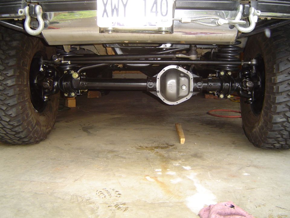 Underside of lifted truck front solid axle with differential, driveshafts, coil springs and mud tires.