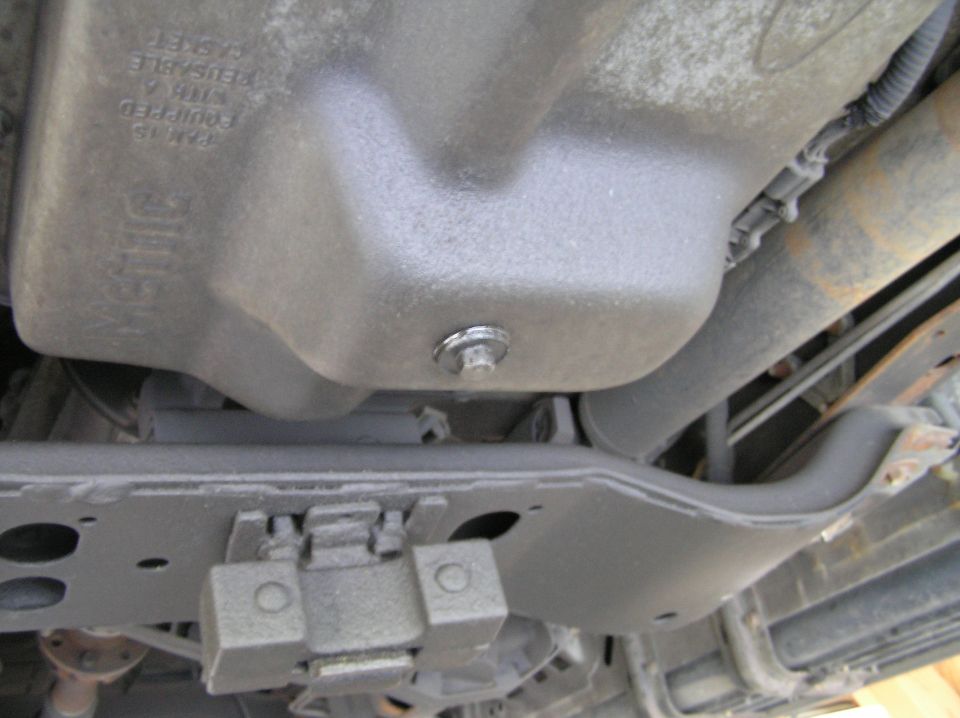 Underside view of vehicle oil pan with drain plug above painted frame crossmember