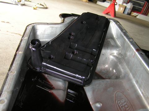 2000 Ford Excursion - A removed transmission pan and filter, showing used fluid and a Ford emblem on the pan.