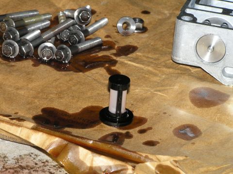 2000 Ford Excursion - A transmission filter and a pile of bolts are laid out on brown paper, stained with oil, suggesting a repair or maintenance task.