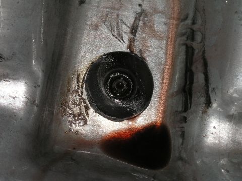 2000 Ford Excursion - Close-up of a transmission pan showing a drain plug and a small amount of dark fluid.