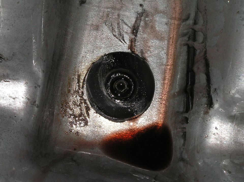 Close-up of a dark drain plug in oily metal surface with brown fluid residue