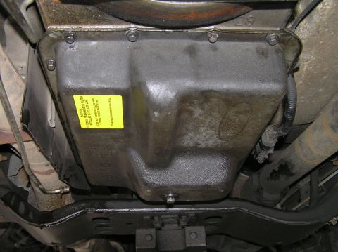 2000 Ford Excursion - Underside view of a transmission pan with a yellow caution sticker indicating an external transmission filter.