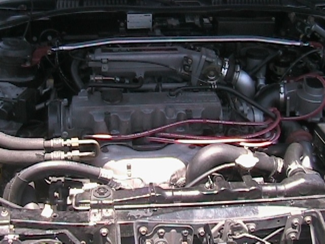 Engine bay of car with red plug wires, strut tower brace, and DOHC valve cover