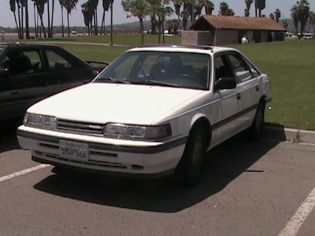 White Mazda 626 sedan parked in lot near palm trees, CA plate 5NQP566