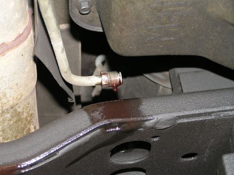 2000 Ford Excursion - Transmission fluid is seen dripping from a metal line onto a black frame component, indicating a potential leak.
