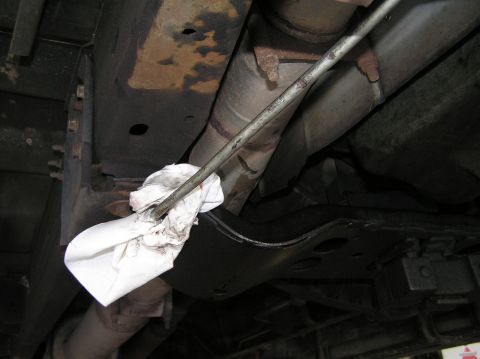 2000 Ford Excursion - A dipstick is being removed from a vehicle's undercarriage, with a rag to catch any drips.
