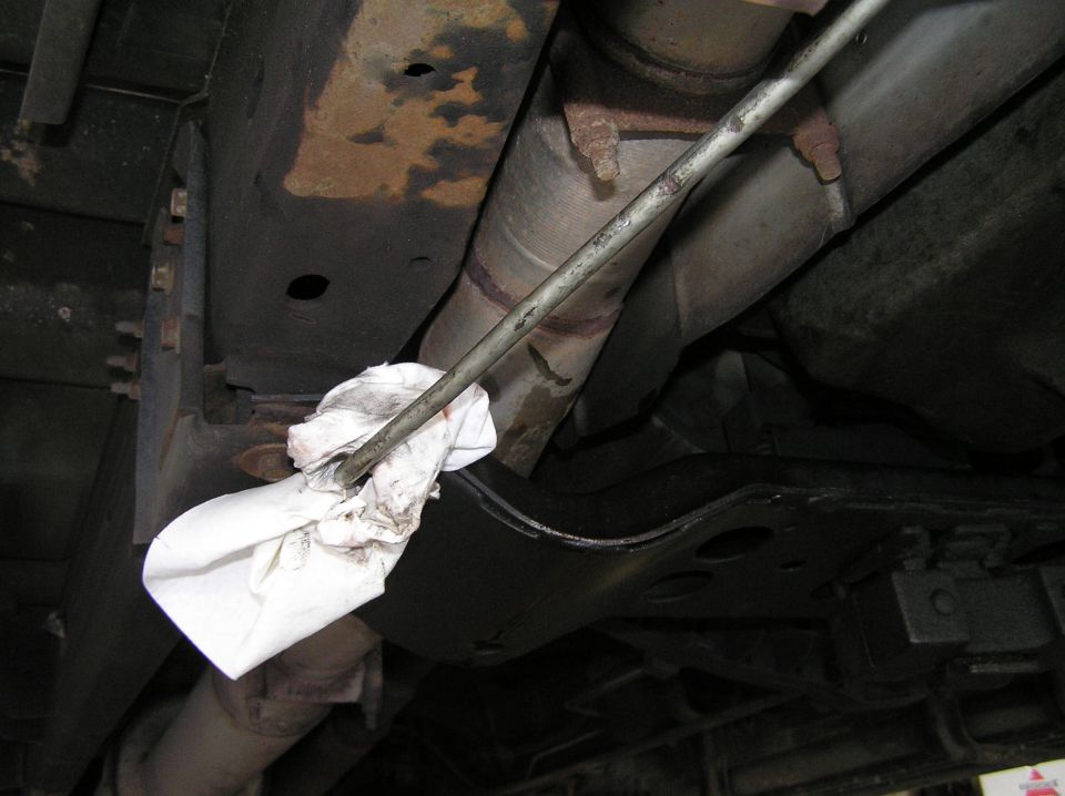 Vehicle undercarriage with rusty exhaust and white rag around a metal rod