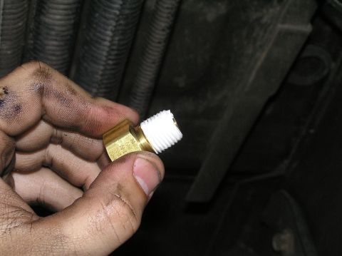 2000 Ford Excursion - A hand holds a brass fitting with white sealant, likely for a transmission filter installation.