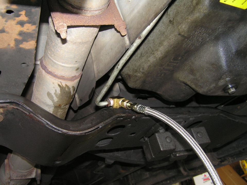 Underbody shot with braided stainless line, brass fittings, rusty exhaust pipe, and black crossmember.