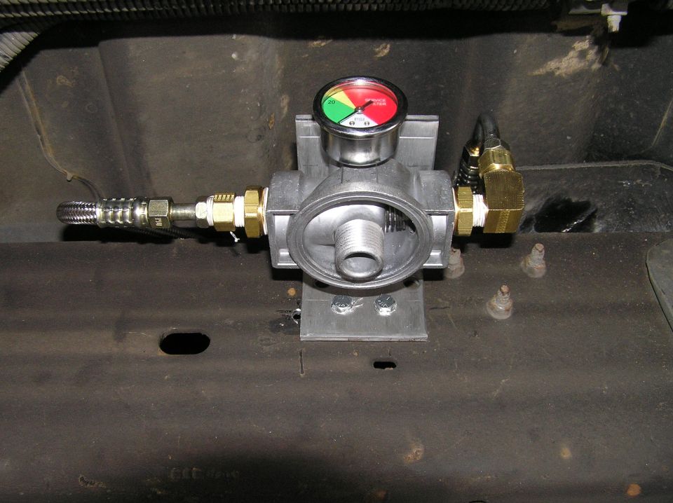 Aluminum fuel filter housing with restriction gauge and brass fittings on a frame rail.