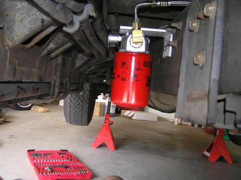 2000 Ford Excursion - A red fuel filter is installed on the underbody of a vehicle, with tools nearby.