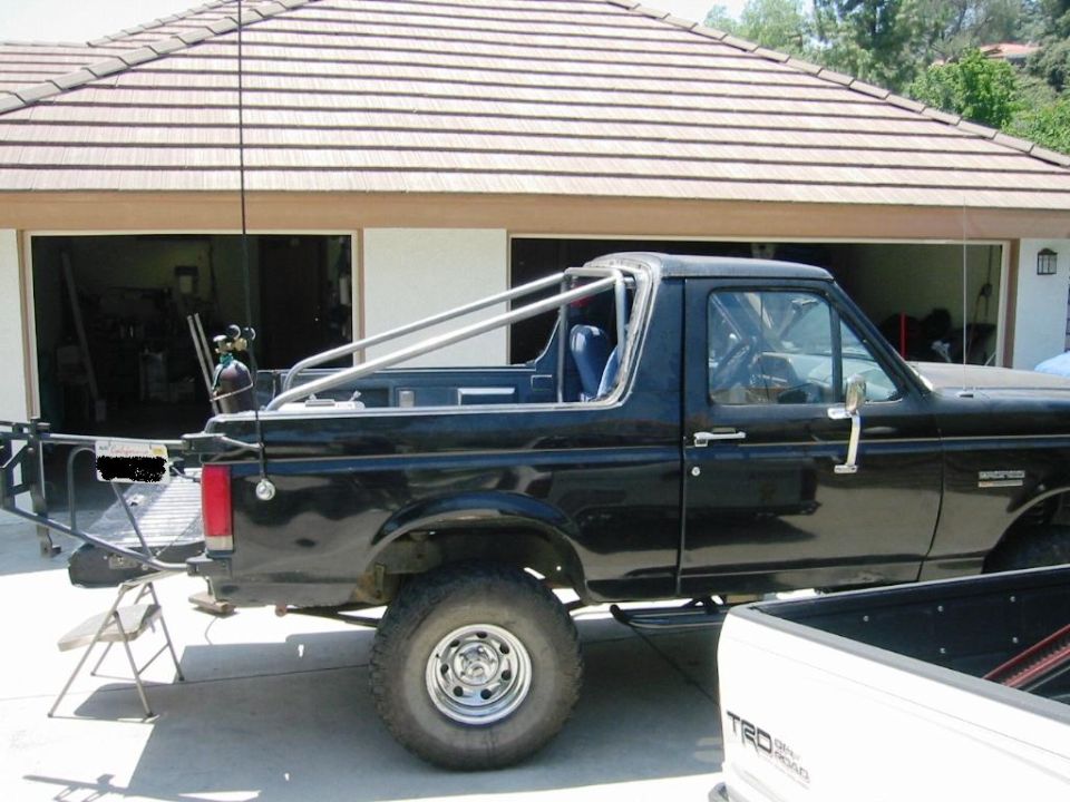 Black lifted Ford Bronco with roll bar and no top, parked by a garage