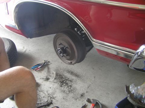 1967 Ford Galaxie - A mechanic works on the brake drum of a red 1967 Ford Galaxie, with tools scattered on the garage floor.