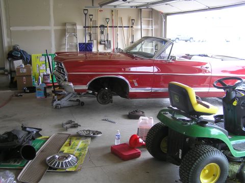 1967 Ford Galaxie - A red 1967 Ford Galaxie convertible is parked in a garage with its front wheel removed, suggesting a brake job is in progress.