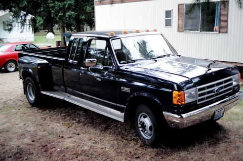 1976 Ford F-150 - This black crew cab dually pickup truck is parked in a grassy area next to a mobile home.