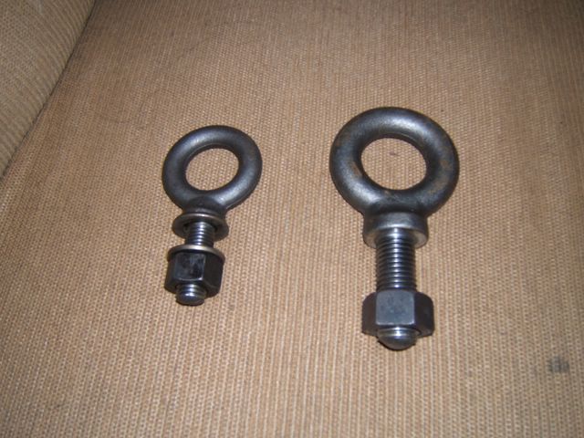 Two metal eye bolts with nuts on a textured brown surface