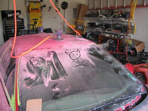 1994 Ford Probe - A car is being worked on in a garage, covered in pink dust with a drawing on the windshield.