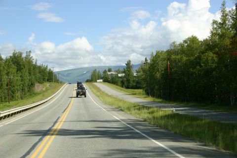 2003 Jeep TJ - Multiple Jeeps travel down a highway surrounded by trees and distant mountains under a cloudy sky.