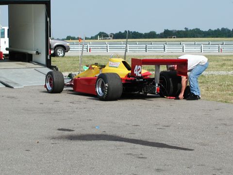 1992 Ford Taurus - A mechanic works on the rear tire of a yellow and red open-wheel race car numbered 42.