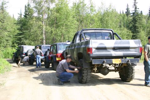 2003 Jeep TJ - A group of off-road vehicles, including a 2003 Jeep TJ and a camouflage pickup truck, are gathered on a dirt road.