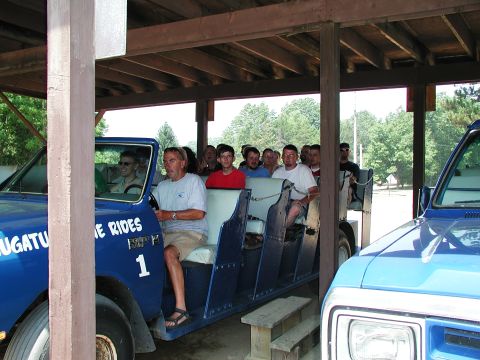 1992 Ford Taurus - A blue passenger vehicle, likely a shuttle, is parked next to another vehicle under a wooden shelter.