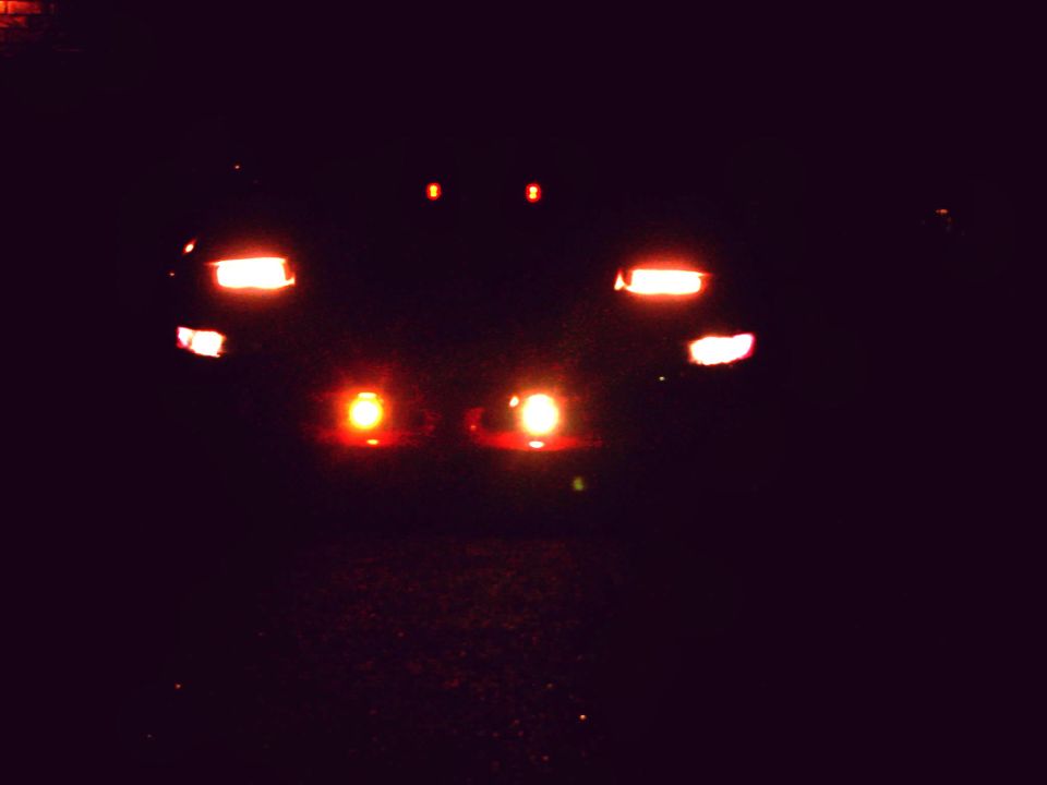 Night shot of a car's front lights glowing in the dark, headlights and fog lamps lit