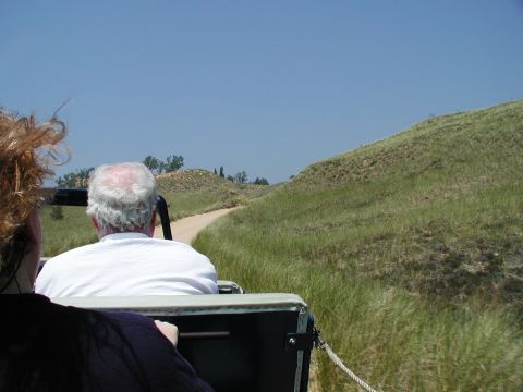 1992 Ford Taurus - Passengers ride in a vehicle on a dirt road through rolling, grassy hills on a sunny day.