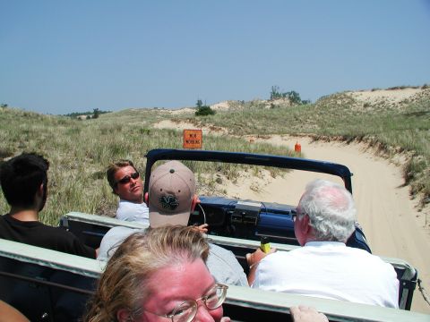 1992 Ford Taurus - Four people ride in a blue Jeep Wrangler on a sandy road through dunes under a clear blue sky.
