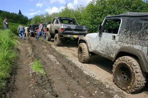 2003 Jeep TJ - Several off-road vehicles, including a Jeep TJ, navigate a muddy track on a sunny day.