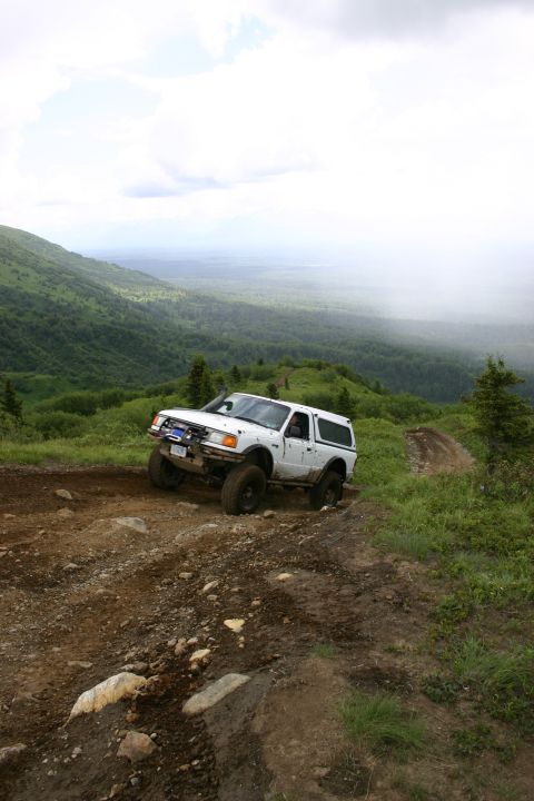 2003 Jeep TJ - A white pickup truck navigates a challenging off-road trail with a scenic mountain vista in the background.