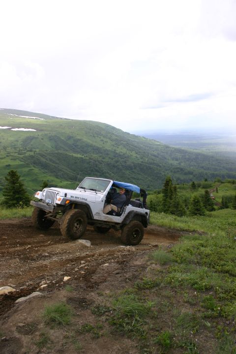 2003 Jeep TJ - A white Jeep Wrangler navigates a steep, muddy incline on a mountain trail under a cloudy sky.