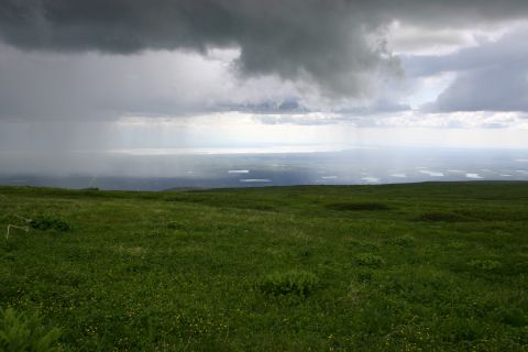 2003 Jeep TJ - A wide view of a green, grassy hill under a dramatic, cloudy sky with rain falling in the distance.
