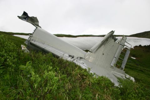 2003 Jeep TJ - Wreckage of an aircraft tail section is visible on a grassy slope, with snow in the background.