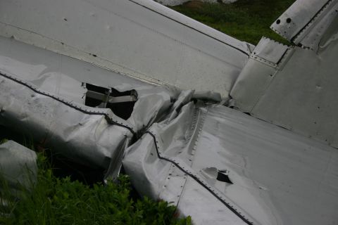 2003 Jeep TJ - The crumpled tail section of an aircraft lies on the ground amidst green foliage.