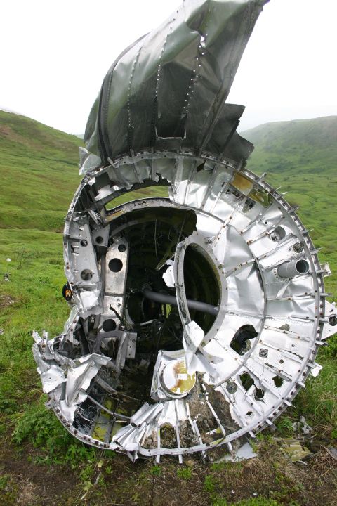 2003 Jeep TJ - The twisted metal and exposed internal structure of a severely damaged aircraft engine nacelle lie on a grassy slope.