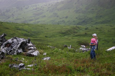 2003 Jeep TJ - A man holds a child while looking out over a vast, green, hilly terrain with scattered debris.