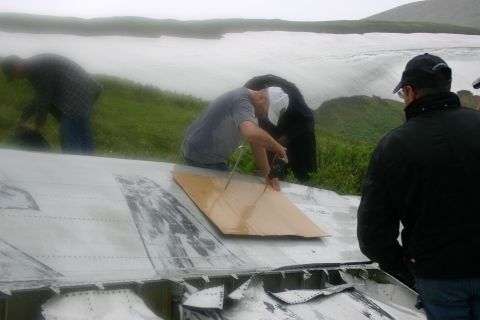 2003 Jeep TJ - Several individuals inspect debris on a hillside, with a large body of water visible in the distance under an overcast sky.