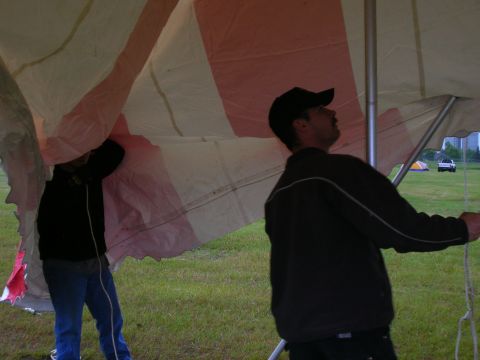 2003 Jeep TJ - Two men work to erect a large striped tent on a grassy field, with two vehicles parked in the distance.