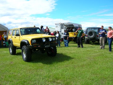 2003 Jeep TJ - Modified yellow Jeep Cherokee XJ at an outdoor event with other vehicles and people.