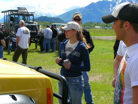 2003 Jeep TJ - A group of people and off-road vehicles are gathered in a field with mountains in the distance.