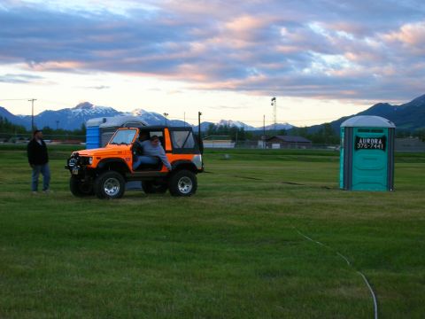 2003 Jeep TJ - An orange off-road vehicle is parked in a grassy field with mountains in the background.