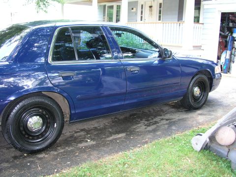 1999 Ford Crown Victoria - A blue sedan is parked on a driveway in front of a house and garage.