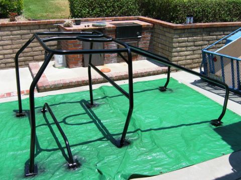 1985 Ford Bronco - A black roll cage is shown on a green tarp in front of a brick outdoor kitchen area.
