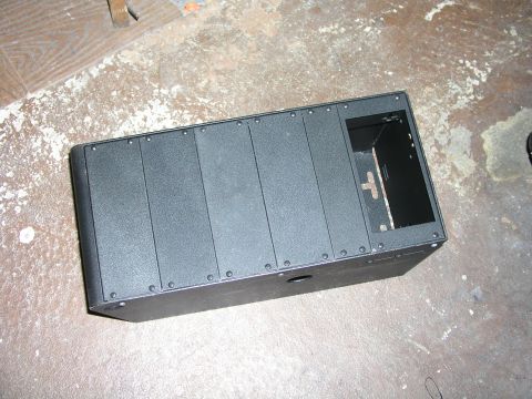 1999 Ford Crown Victoria - A black console unit with a textured surface and visible rivets sits on a worn concrete floor.