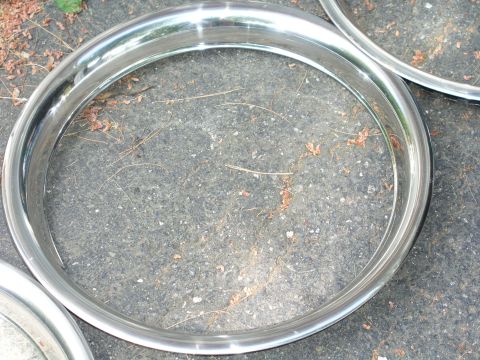 1999 Ford Crown Victoria - A close-up view of two chrome trim rings resting on an asphalt surface with scattered leaves.
