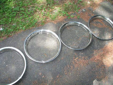 1999 Ford Crown Victoria - Four chrome trim rings are laid out on a paved surface next to grass.