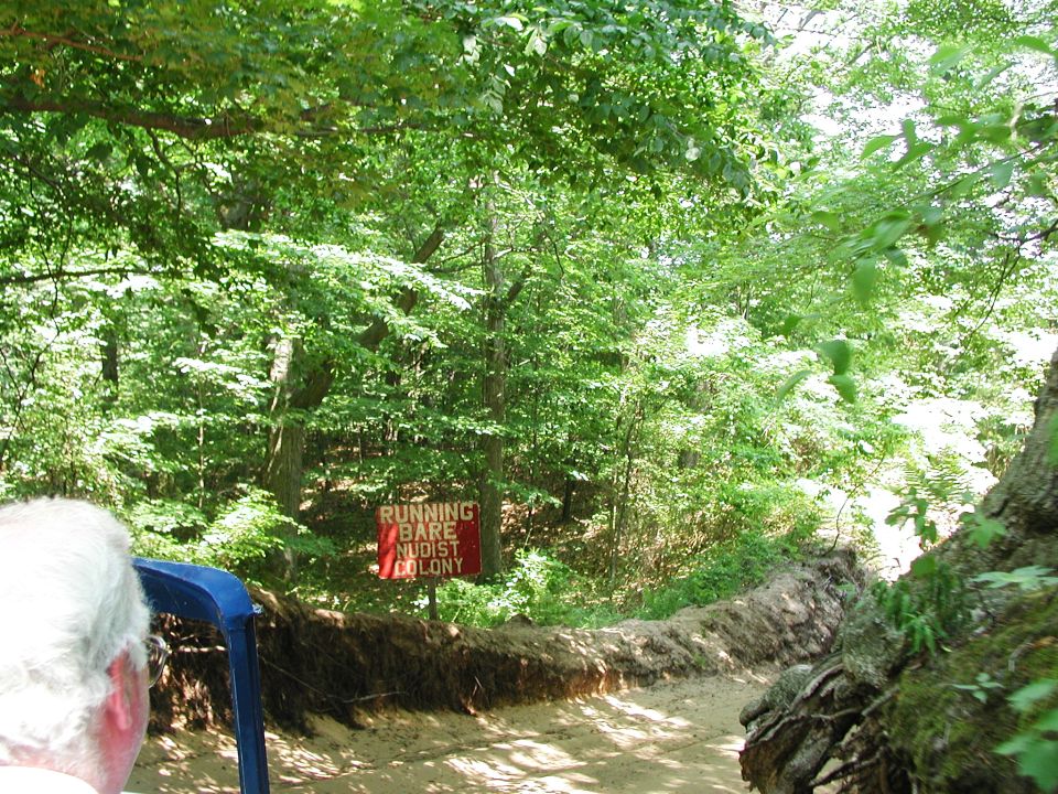 Dirt path through trees with a sign for 'RUNNING BARE NUDIST COLONY'