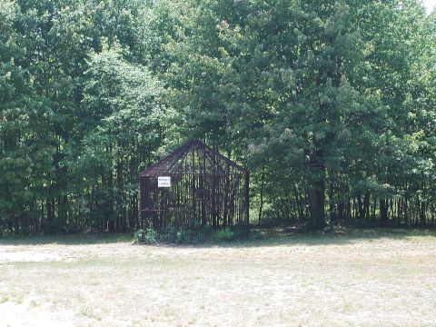 1992 Ford Taurus - A rustic cage structure stands in a grassy field, surrounded by dense trees.